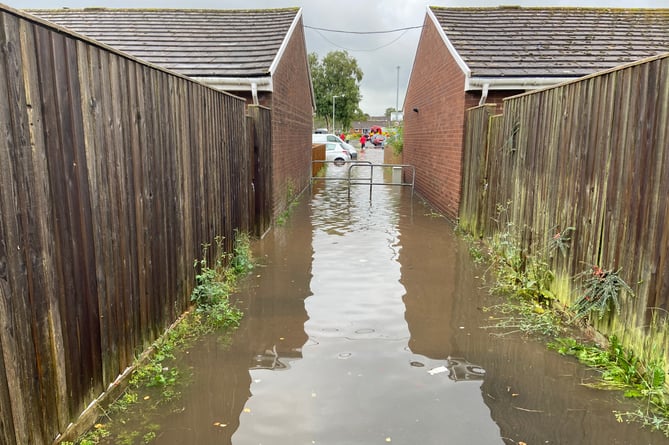 A walkway into Bovet Street under several inches of water after a rainstorm last September, with emergency services personnel visible in the distance evacuating tenants.