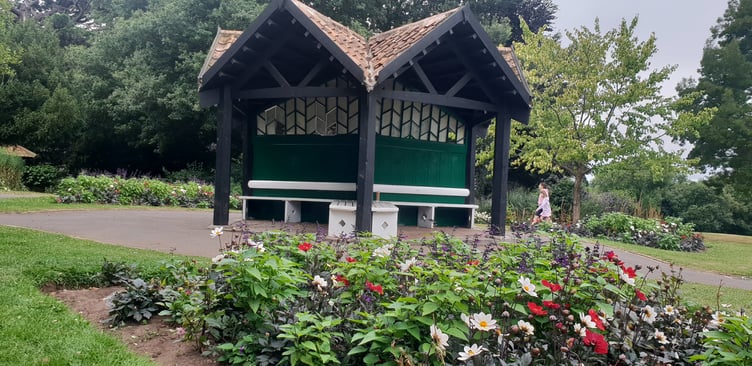 A view of the 'thrupenny' shelter surrounded by flower beds in Wellington Park.