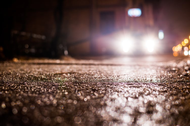 Rainy night in the big city, glare from the headlights of the parked car. Close up view from the sidewalk level