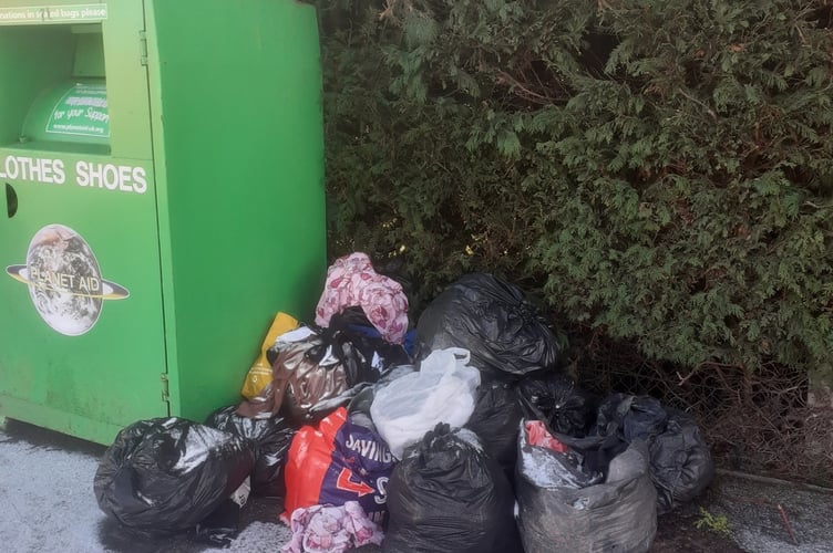 Piles of clothes next to the clothing donation bin.